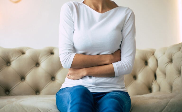 Woman experiencing abdominal pain while sitting on couch – chronic pain treatment in San Antonio