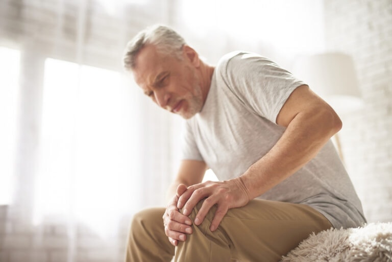 Man sitting indoors holding his knee due to chronic joint pain.